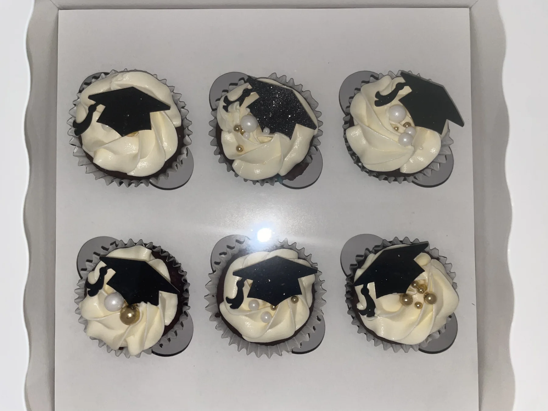 Six white graduation cupcakes decorated with black caps