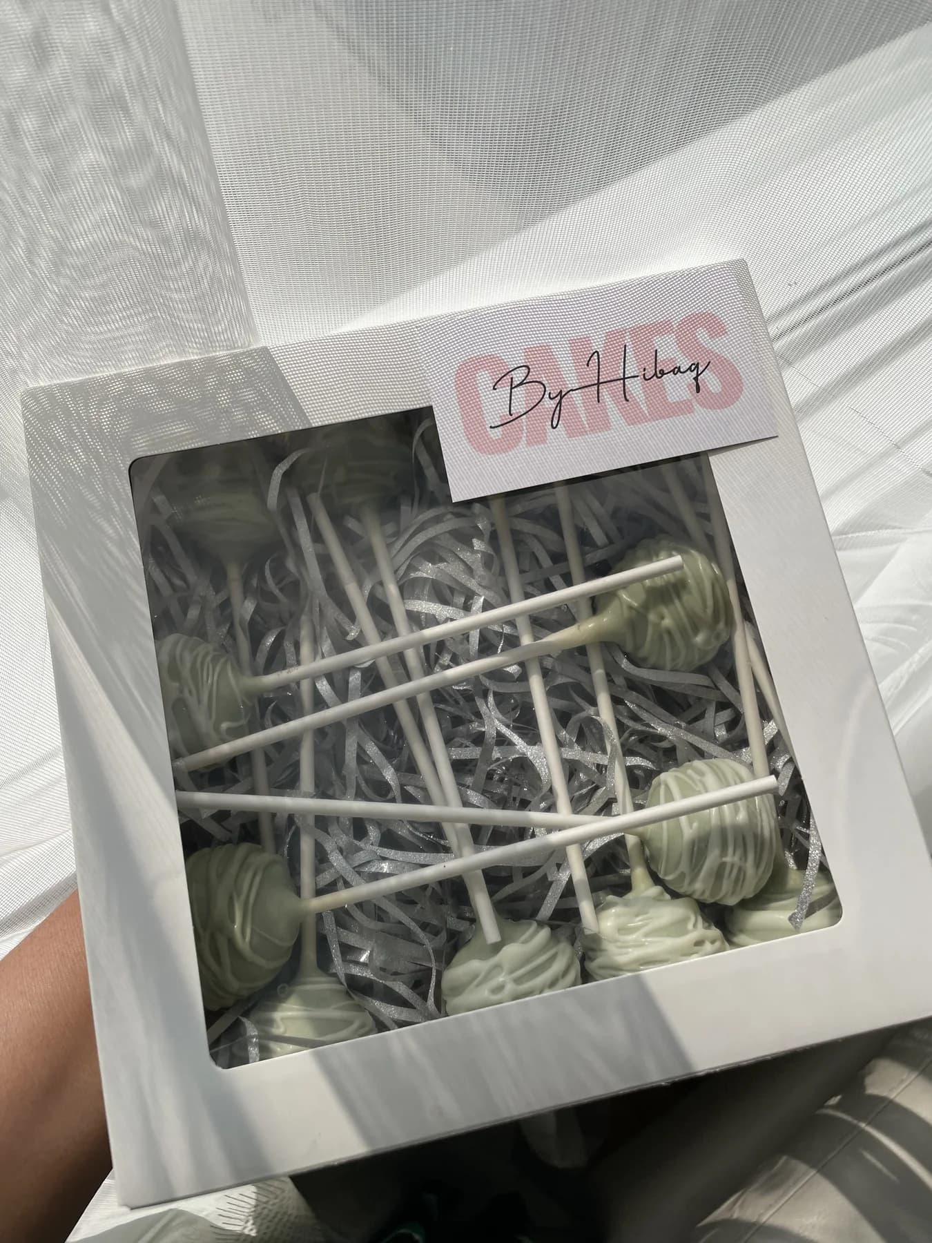 Green cake pops drizzled with white chocolate in a branded window box