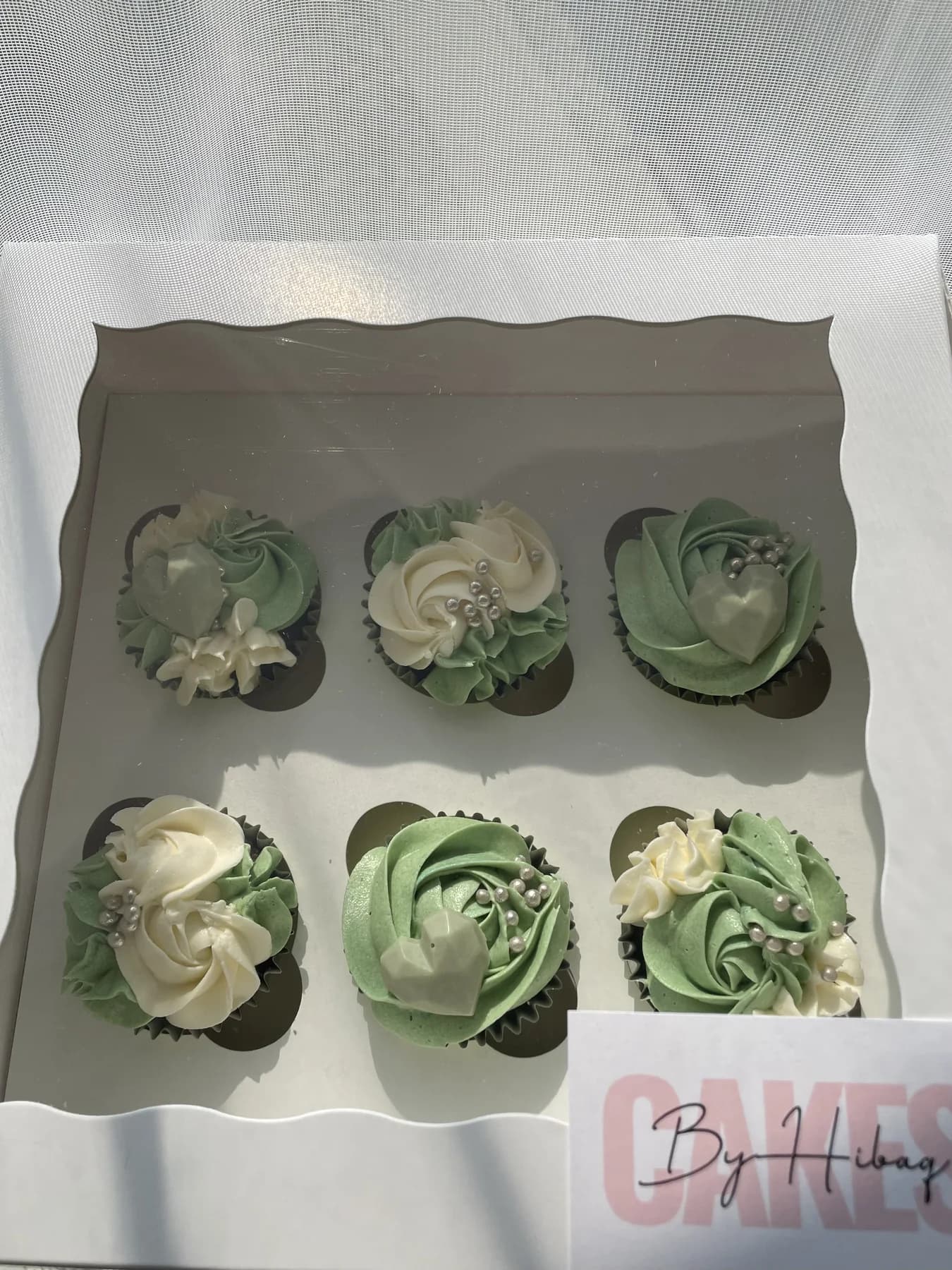Green and white cupcakes presented with a Cakes by Hibaq card